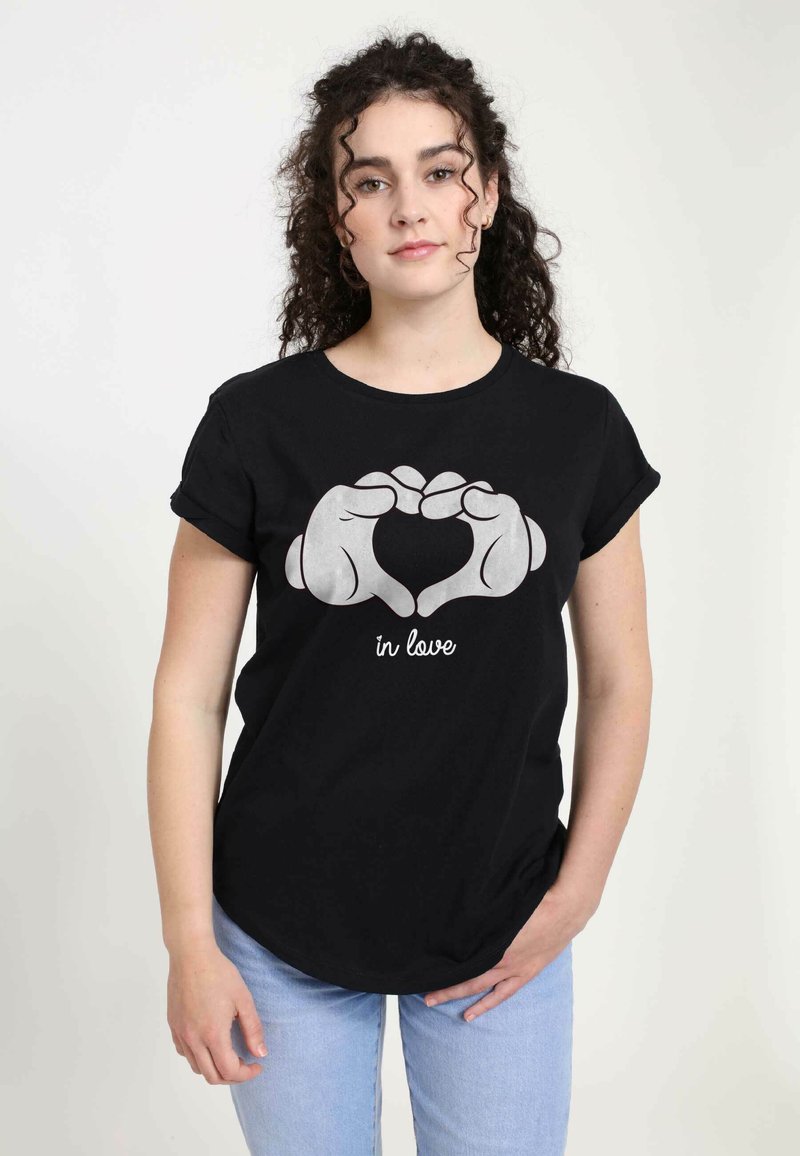 Sort bomulds T-shirt med et sølvfarvet grafisk motiv af hænder, der danner et hjerte, ledsaget af teksten "in love" under designet.