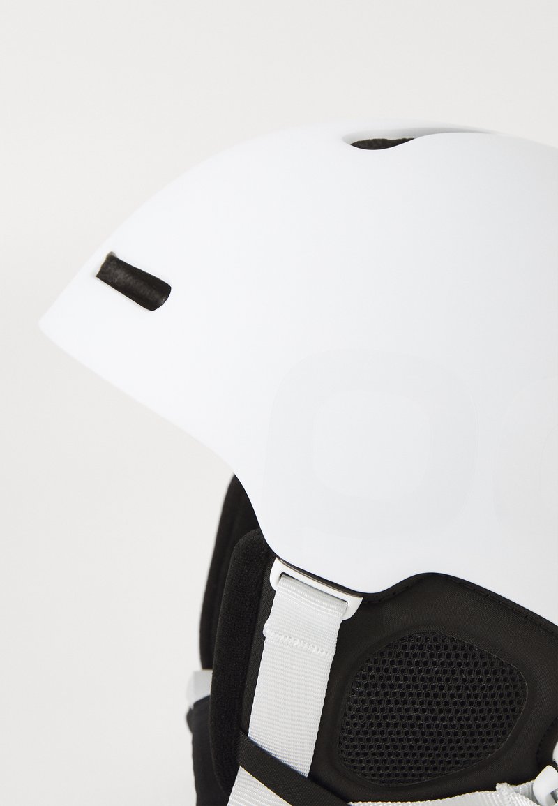 Weißer Skihelm mit glatter Oberfläche, Luftöffnungen und schwarzer Innenpolsterung. Verfügt über einen grauen verstellbaren Riemen und unterstützendes Zubehör.