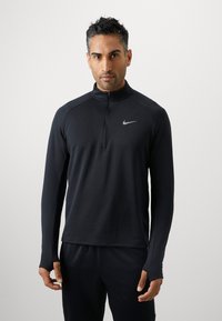 Crni sportski pulover s munjevitim ovratnikom, strukturom tkanine, dugim rukavima i malim srebrnim Nike logom na lijevoj strani prsa.