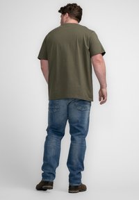 Camiseta de algodón verde oliva combinada con jeans de mezclilla azul. La camiseta tiene un ajuste holgado, mangas cortas y un diseño de cuello redondo.