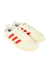 Baskets en cuir blanc avec trois bandes rouges, une semelle en caoutchouc crème et un bout perforé pour la respirabilité. Lacets inclus.