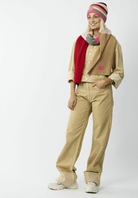 Chemise et pantalons en velours côtelé beige oversize, superposés avec une écharpe tricotée multicolore et un bonnet rayé. Des baskets blanches complètent le look.
