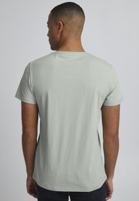 Tricou scurt de culoare verde deschis, cu mânecă scurtă și guler rotund. Material din bumbac moale, croială lejeră și design minimalist. Textură netedă fără modele.