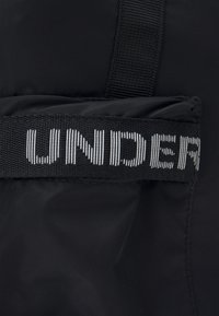 Czarna torba z materiału o fakturowanej powierzchni, z wyraźnym paskiem oznaczonym napisem "UNDER" w białym detalach wzoru.