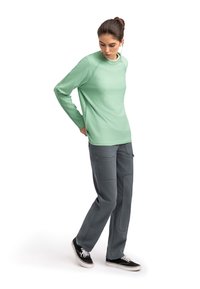 Camicia a maniche lunghe verde chiaro con maniche raglan abbinata a pantaloni cargo grigi con tasche, indossata con sneakers nere.
