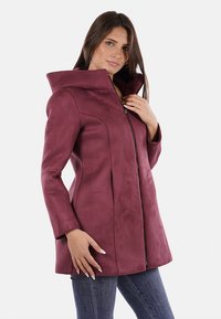 Cappotto borgogna con cappuccio, dalla texture liscia, chiusura con zip, design strutturato e maniche lunghe, indossato sopra jeans blu.