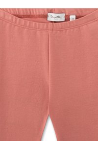 Hellrosa Leggings aus weichem Material mit glatter Textur, ausgestattet mit einem elastischen Bund und ohne sichtbare Nähte. Markenetikett innen.