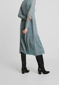 Sukienka z długim rękawem w jasnoniebieskim kolorze z drobnym brązowym wzorem kwiatowym, z falbanowym dołem, poł�ączona z czarnymi botkami na obcasie.