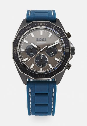 Montre chronographe noire et bleue avec un bracelet en caoutchouc bleu texturé, un cadran gris, trois sous-cadrans et des index horaires blancs, dotée d'une échelle tachymétrique.
