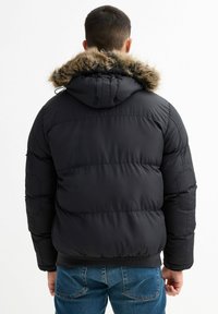 Abrigo de invierno acolchado negro con capucha de piel sintética desmontable. Presenta puños y dobladillo acanalados, con una textura suave y brillante.