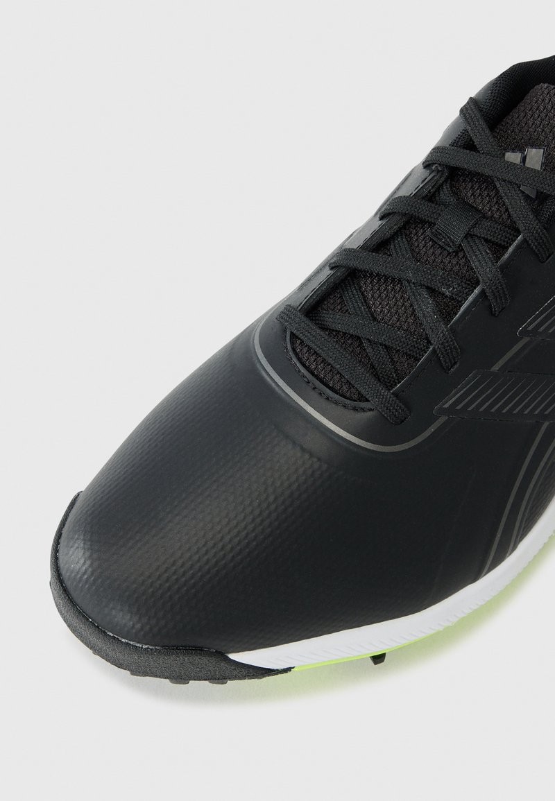 Schwarzer Sportschuh mit einem schlanken synthetischen Obermaterial, strukturierten Details und einer kontrastierenden weißen und neon-grünen Sohle. Verfügt über ein Schnürsystem.