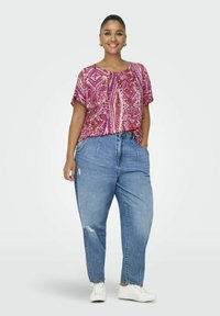 Blouse à manches courtes rose et violette à motifs associée à un jean léger en denim déchiré et à des baskets blanches, offrant une coupe décontractée et un style casual.