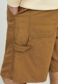 Pantaloni scurți cargo maro cu o croială lejeră, prezentând buzunare laterale și un material texturat. Detalii distincte de cusătură și un buzunar aplicat în spate.
