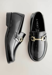 Mocassins en cuir noir poli avec un accent en matériel doré et une caractéristique de sangle. Bout arrondi et semelle en caoutchouc texturée basse.