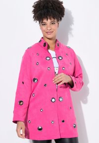 Růžová semišová bunda s kulatými černými a stříbrnými očky, zapínáním na knoflíky a límcem. Dlouhé rukávy a volný střih.