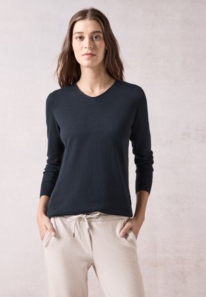 Maglione nero a maniche lunghe con scollatura rotonda, realizzato in un tessuto a maglia liscio, abbinato a pantaloni della tuta beige chiaro con cordino.