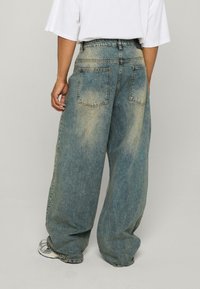 Hellblaue, übergroße Denim-Jeans mit hoher Taille, ausgestattet mit zwei Gesäßtaschen und einer ausgewaschenen Textur. Lockere Passform und weiter Beinschnitt.