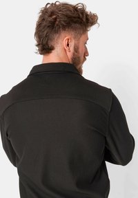 Zwarte geribde shirt met kraag, gemaakt van een gestructureerde stof en met een contrasterend schouderpaneel, gezien vanaf de achterkant.