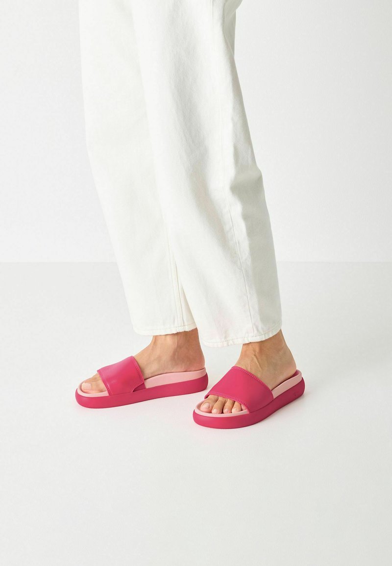 Rosa halksandaler med en bred rem och en dämpad sula. Designen har en tjock, solid bas och en öppen tå.