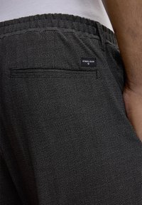 Pantalon de jogging gris texturé avec une taille élastique. Il dispose d'une poche arrière et d'une étiquette noire avec du texte blanc.