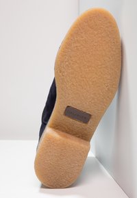 Suela de zapato de ante azul marino con un acabado texturizado, que presenta una base de goma marrón claro y un pequeño parche de logo marrón grabado con "HILFIGER".