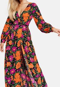 Robe maxi florale avec un fond noir et des fleurs orange et roses vives, manches longues, décolleté en V profond et une fente sur le côté.
