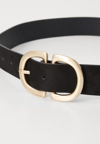 Cintura in pelle nera con superficie texturizzata e fibbia a doppio ardiglione color oro con finitura liscia. Regolabile con più fori.