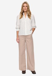 Witte blouse met kleine bloemenprint, pofmouwen en knoopsluiting, gecombineerd met beige wijde-broekspijpen en donkerbruine laarzen.