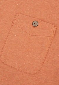 Orangener strukturierten Stoff mit einer kleinen Brusttasche. Die Tasche hat einen abgerundeten Deckel und einen braunen Knopf zum Schließen. Dezente Sprenkel im Material.