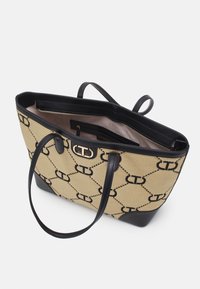 Sac tote avec un extérieur tissé beige présentant un motif de logo noir, des accents en cuir noir et des poignées doubles. L'intérieur comprend une poche zippée.