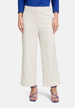 Cremefarvede bukser med bredt ben, der har en glat tekstur og frontlommer, parret med blå strophæle. Outfitet har en blå top.
