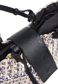 Borsa intrecciata realizzata con una combinazione di fibre naturali e accenti blu, con una tracolla in pelle nera e un'etichetta testurizzata in evidenza.