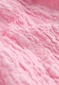 Tissu rose froissé avec une surface texturée, présentant des vagues douces et irrégulières ainsi qu'un léger brillant sur le matériau.