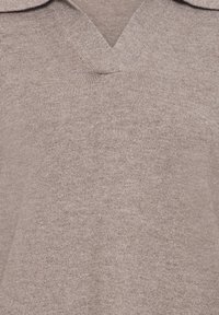 Gros plan d'un pull beige en maille côtelée avec col en V et détail de tissu texturé.