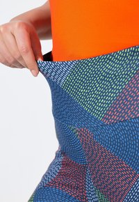 Ropa deportiva multicolor con patrones geométricos; presenta una parte superior naranja y unas mallas azul con estampados y acentos en verde y rojo. Tela elástica.