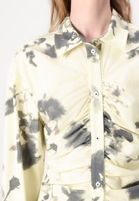 Yellow blouse with black watercolor-like patterns, featuring a button-up front, collar, and gathered detail along the sides and front.