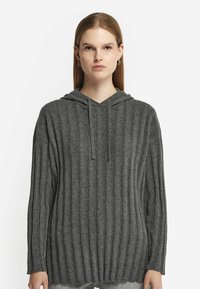 Szary sweter z kapturem, o pionowym prążkowanym wzorze, długich rękawach i dekolcie w kształcie litery V. Materiał wydaje się miękki i lekko fakturowany. Zaprojektowany w luźnym fasonie.