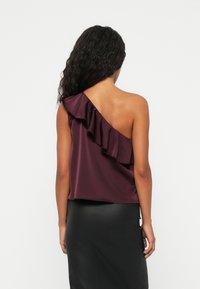 Burgundy satin topp med en asymmetrisk design, som har en enda axelruche och en mjuk textur, kombinerad med en åtsittande svart kjol.