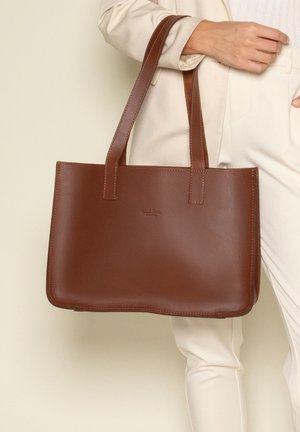 Brun læder tote taske med rektangulær form, flad bund og to robuste håndtag. Har et præget logo på forsiden og en glat tekstur.
