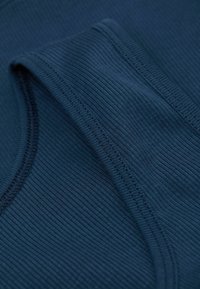 Marinblå ribbat tyg med en slät yta, med en rund halsringning och sydda kanter som visar upp lager av veck.