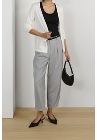 Cardigan bianco aperto davanti sopra un top nero, abbinato a pantaloni plissettati grigi chiari e tacchi slingback neri. Dettaglio della borsa nera in evidenza.