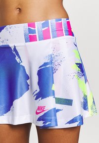 Falda deportiva de mujer de Nike en blanco, con un patrón abstracto colorido en azul, rosa y verde neón, con una textura de malla y detalle de logo.
