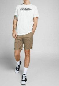 Bílá tričko s grafickým potiskem, khaki šortky, bílé ponožky, černé tenisky. Neformální outfit; šortky jsou ohrnuté na lemu.