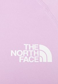 Světle fialová tkanina s hladkou texturou a bílým logem "THE NORTH FACE" s zakřiveným akcentovým designem.