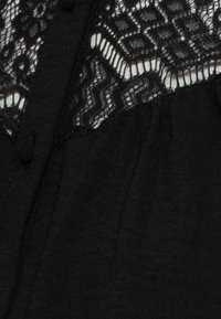 Svart blus med en övre del av intrikat spets med ett geometriskt mönster, mjuk textur och knapprad längs framsidan.