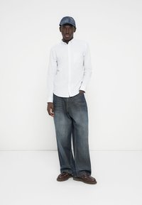 Ανοιχτό μπλε ριγωτό πουκάμισο με μακριά μανίκια, άνετο σκούρο μπλε τζιν παντελόνι και σκούρο μπλε καπέλο. Καφέ παπούτσια με κορδόνια. Απλός σχεδιασμός, καθημερινή ενδυμασία.