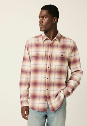 Karierte Hemd in Schattierungen von Lila, Creme und Braun; verfügt über zwei Brusttaschen und eine Knopfleiste vorne; aus strukturiertem Stoff gefertigt.