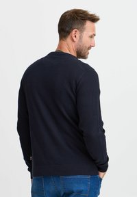 Strikket marineblå genser med rund hals og ribbede mansjetter. Har et strukturert mønster og en logo nederst. Ryggvinkel vist.
