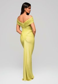 Off-the-shoulder, pitkä helmainen mekko metallinhohtoisessa keltaisessa, joka sisältää kerroksittain somistettuja yksityiskohtia ja taskuja, tiukassa siluetissa ja sileässä pinnassa.