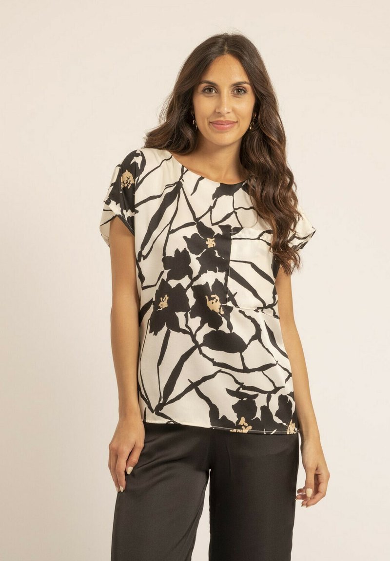 Blouse à motif floral en crème avec des accents noirs et dorés. Manches courtes, coupe décontractée, texture lisse et col rond.